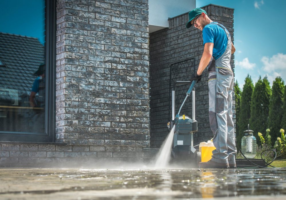 Pressure Washer Cleaning Pressure Washer Cleaning in Front of the House. Caucasian Men in His 30s Washing Concrete Bricks Driveway in Sunny Summer Day. Cleaning Around the House Concept.